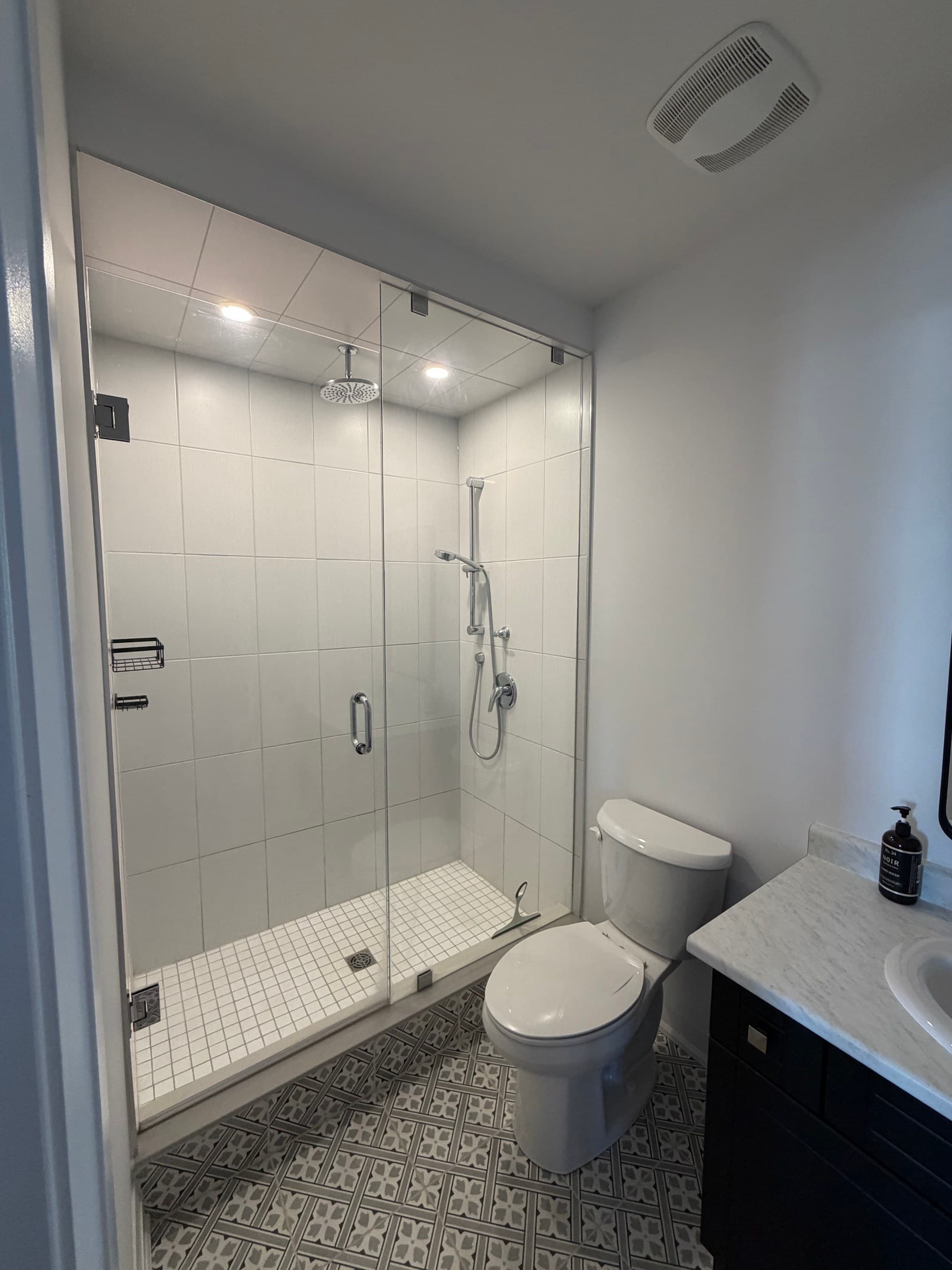Finished bathroom renovation with glass shower enclosure and patterned tile floor by Everline Plumbing in Toronto