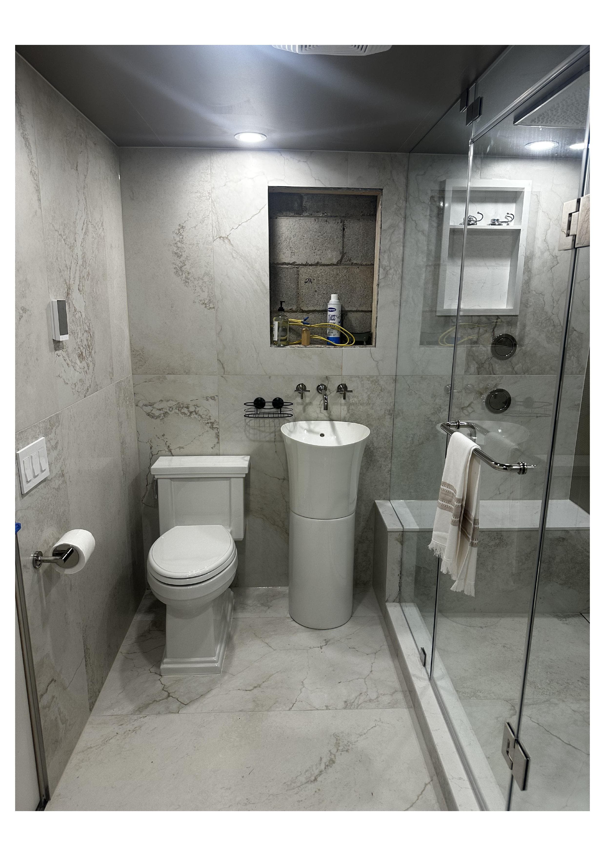 Completed bathroom with pedestal sink, toilet, and glass shower niche